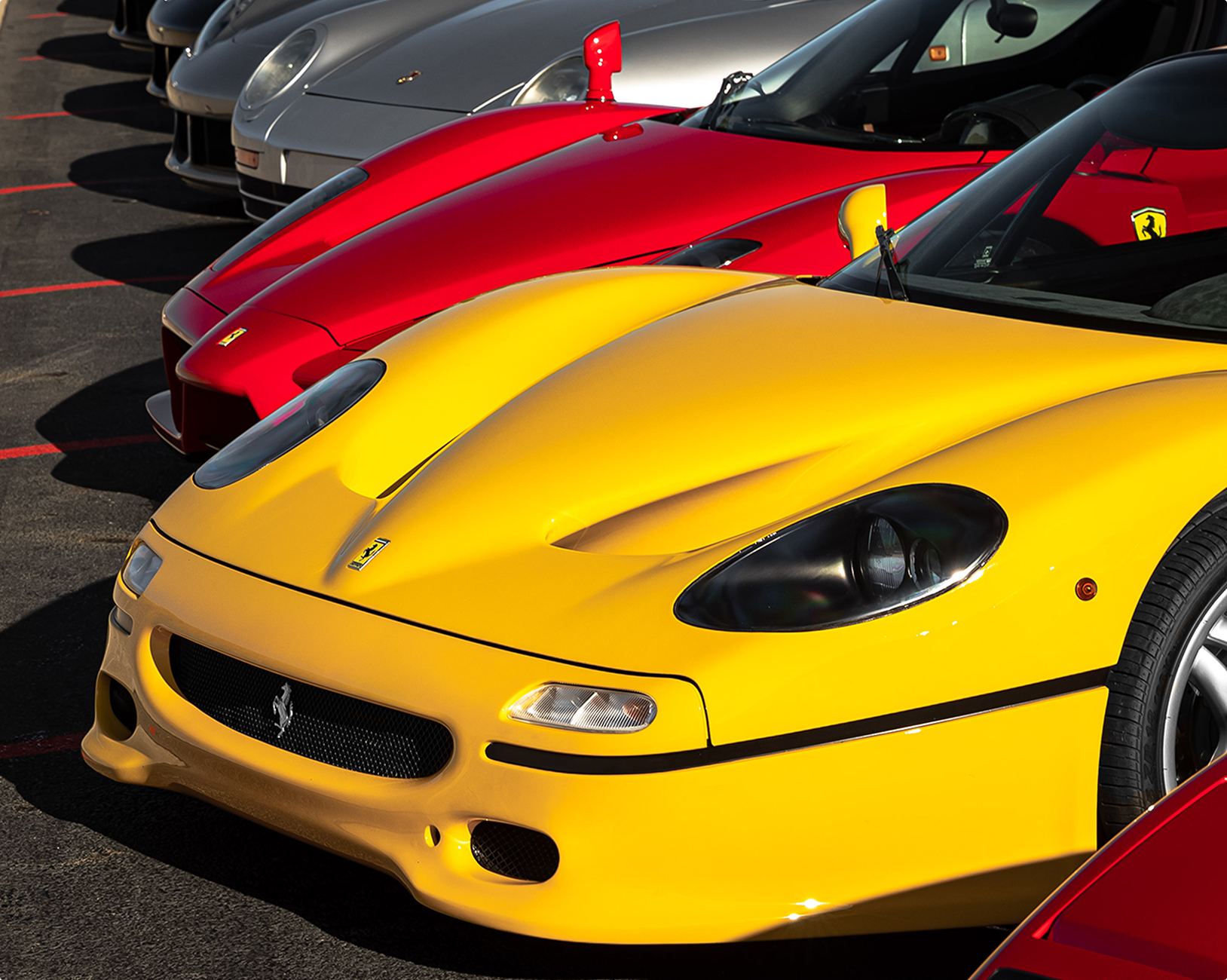Line of exotic cars parked diagonally including yellow Ferrari F50, Red Ferrari Enzo, Silver Porsche 959