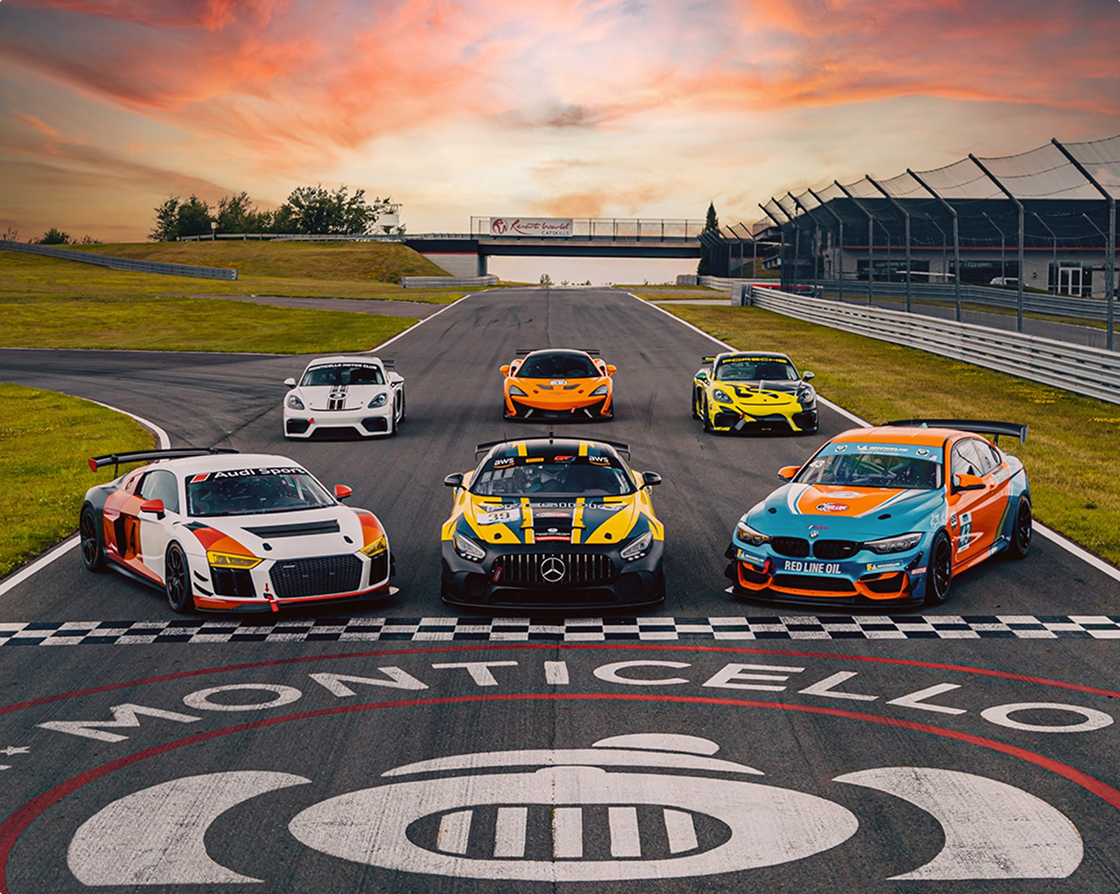 Six race cars parked on a race track at the finish line with a sunset in the background. The cars are all GT4 - Audi R8, Mercedes AMG, BMW M4, 2x Porsche 718 Clubpsort, McLaren 570S