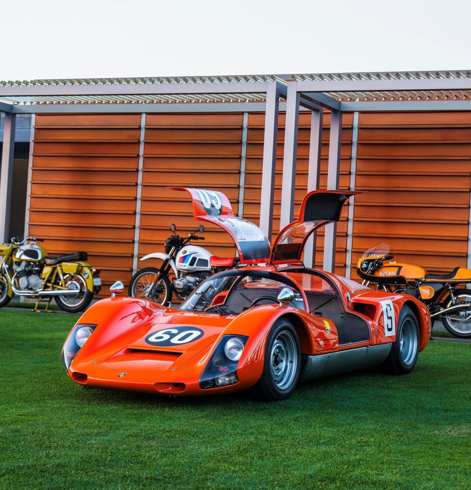 Orange Porsche 906 on a lawn with doors open