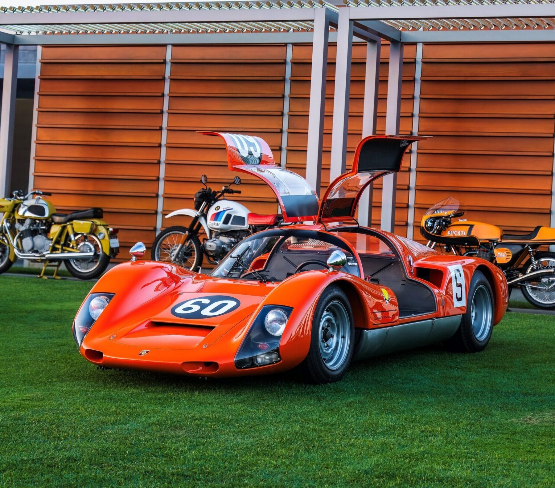 Orange Porsche 906 on a lawn with doors open