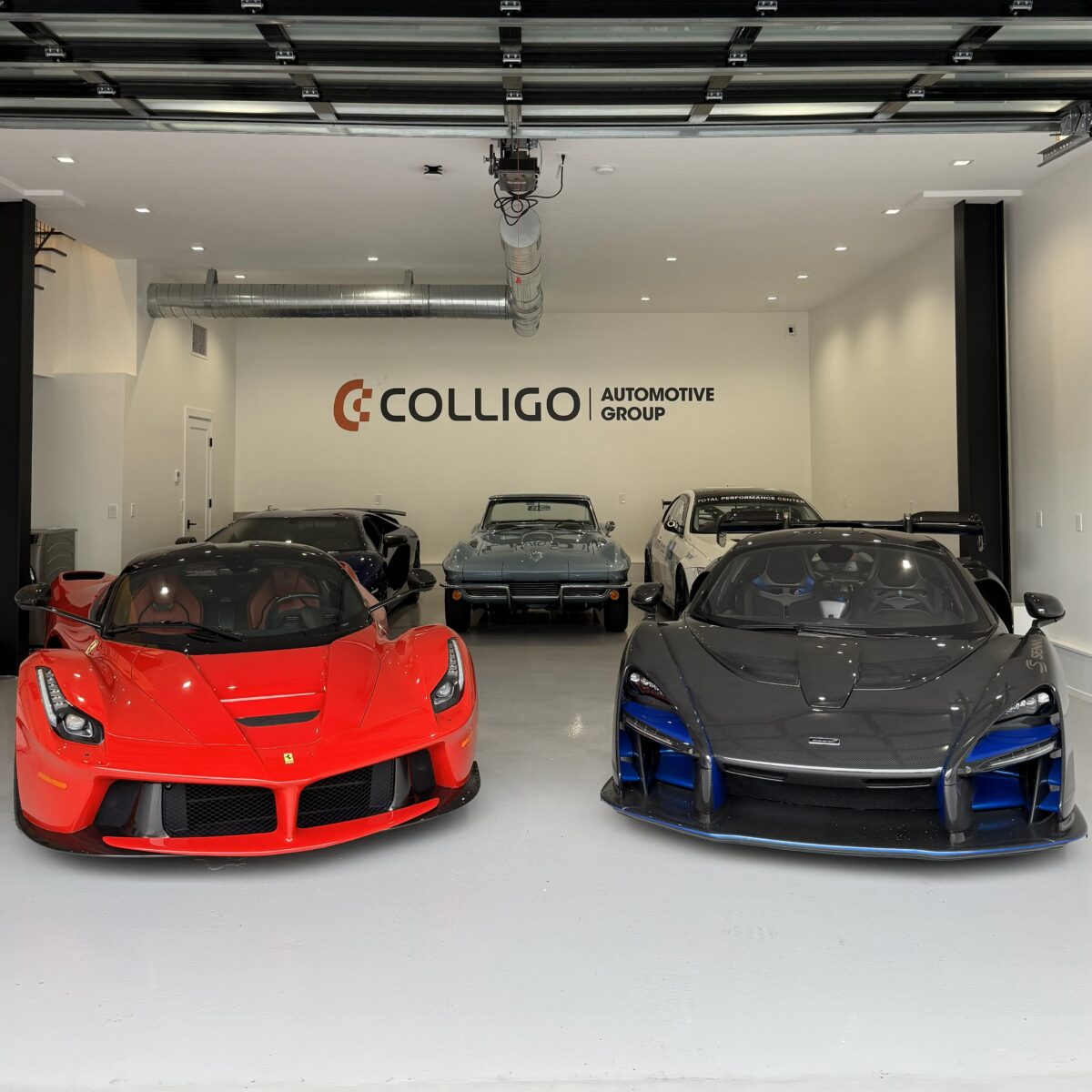 five vehicles in a garage with white walls and Colligo Automotive Group on the back wall. Red Ferrari LaFerrari and black McLaren Senna in back row. Blue lamborghini aventador, blue chevy corvette, and bmw m3 in back row